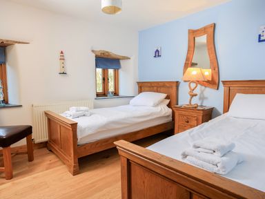 A bedroom with two single wooden beds and a nightstand with a lamp at Cowslip Cottage in Frogmore