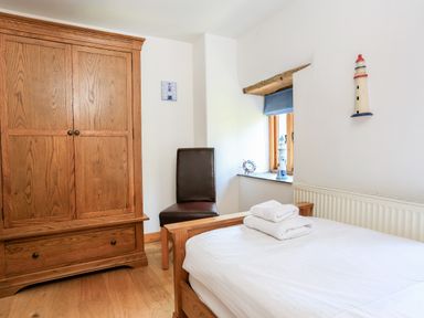 A bedroom with a wooden wardrobe a bed with towels a chair and window decorations at Cowslip Cottage in Frogmore