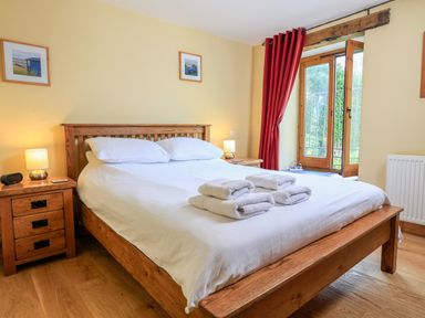 A bedroom with a wooden bed frame white bedding folded towels bedside tables lamps and framed pictures at Cowslip Cottage in Frogmore