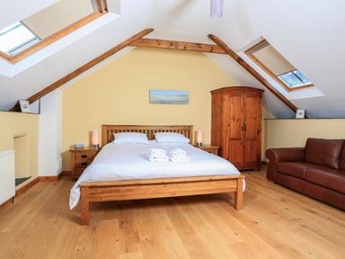 A bedroom with a wooden bed white bedding wooden furniture skylights and a brown leather sofa at Cowslip Cottage in Frogmore