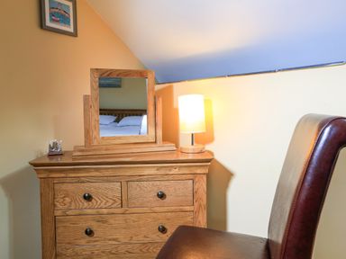 A wooden dresser with a mirror a lamp and a brown chair in a bedroom at Cowslip Cottage in Frogmore