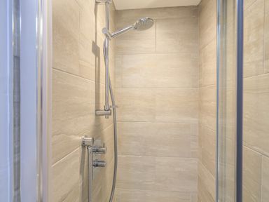 A shower area with beige tiles and a chrome showerhead in a bathroom at Cowslip Cottage in Frogmore