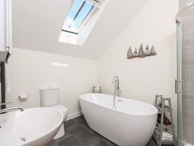 A bathroom with a bathtub toilet sink skylight and shelf with towels and plants at Cowslip Cottage in Frogmore