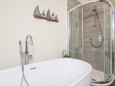 A bathroom with a freestanding bathtub and a glass shower enclosure with a metal showerhead at Cowslip Cottage in Frogmore