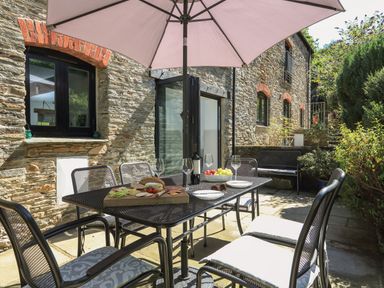 An outdoor dining area with a table set with food, wine, glasses, and chairs under an umbrella at Cowslip Cottage in Frogmore