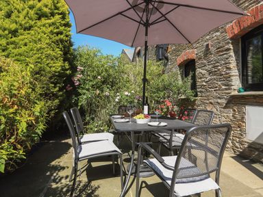An outdoor patio with a dining table and six chairs under an umbrella at Cowslip Cottage in Frogmore