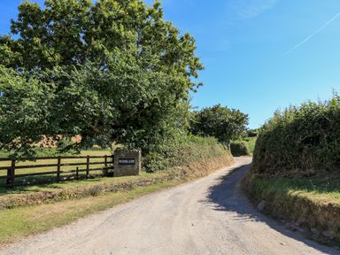 A country dirt road lined with hedges and a tree next to a stone sign saying Winslade