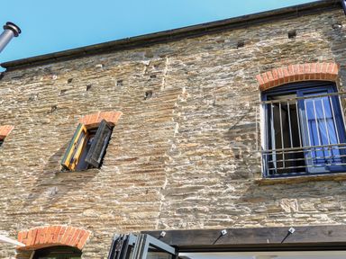 A stone building exterior with open windows and a metal railing under a clear sky at Cowslip Cottage in Frogmore
