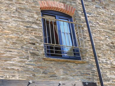 A stone wall with a window that has blue frame and metal bars at Cowslip Cottage in Frogmore