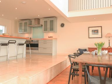 A kitchen with bar stools and a dining table with chairs and flowers at Sea Peep in Thurlestone