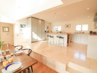 A kitchen area with an island and stools next to a dining table with plates and glasses at Sea Peep in Thurlestone