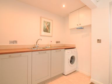 A utility room with a sink washing machine wall cabinets and a framed picture at Sea Peep in Thurlestone