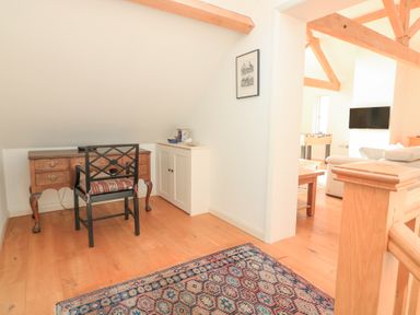 A corner with a wooden desk and chair a white cabinet and a patterned rug on a wooden floor at Sea Peep in Thurlestone