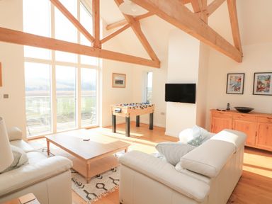 A living room with white sofas wooden beams foosball table and large windows at Sea Peep in Thurlestone