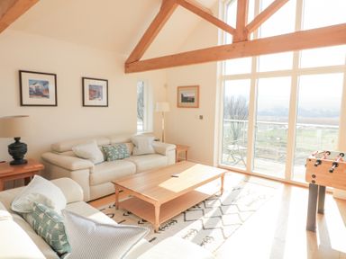 A living room with two sofas a wooden coffee table foosball table and large windows at Sea Peep in Thurlestone