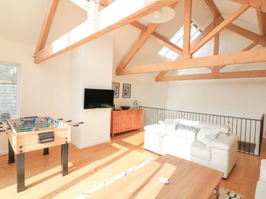 A room with wooden beams on the ceiling a foosball table a wall-mounted television a wooden cabinet and a white sofa at Sea Peep in Thurlestone