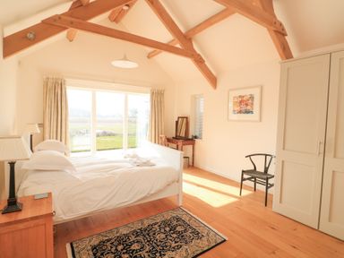 A bedroom with a bed bedside tables a wardrobe a chair a vanity table and large windows overlooking a garden at Sea Peep in Thurlestone