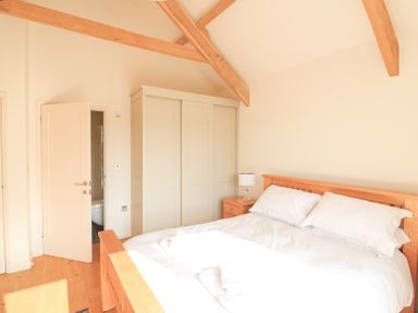 A bedroom with a wooden bed white bedding a bedside table with a lamp a wardrobe and an open door showing a bathroom at Sea Peep in Thurlestone