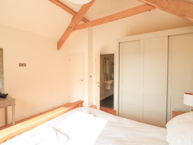 A bedroom with wooden ceiling beams a bed with white bedding a gray wardrobe and an open door to a bathroom at Sea Peep in Thurlestone