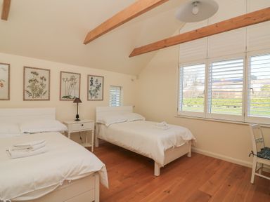 A bedroom with two white beds wooden beams and botanical prints on the wall at Sea Peep in Thurlestone