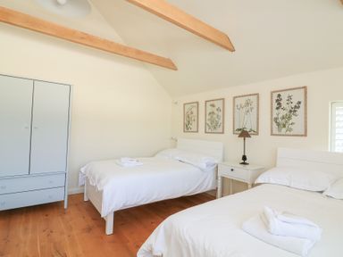A bedroom with two beds white linens a white wardrobe wooden floor and floral wall art at Sea Peep in Thurlestone