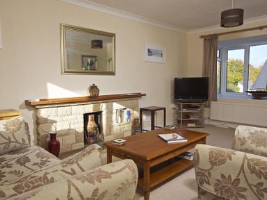 A living room with floral patterned sofas a wooden coffee table fireplace and a TV on a stand at Amberley in Dartmouth