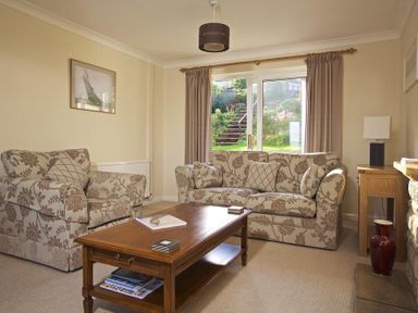 A living room with patterned sofas a wooden coffee table and a window with garden view at Amberley in Dartmouth