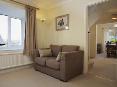 A living room with a brown sofa and floor lamp next to a window and dining room visible through a doorway at Amberley Dartmouth