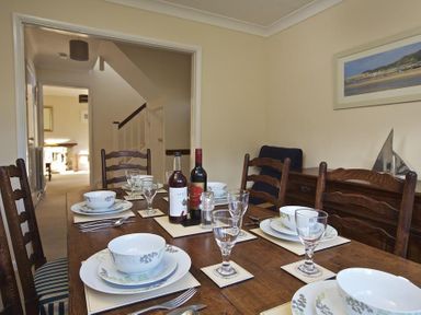 A dining table set with plates bowls glasses and bottles in a dining room with wooden chairs at Amberley in Dartmouth
