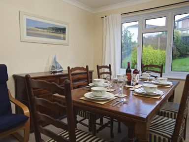 A dining room with a wooden table set with bowls glasses and cutlery near a window at Amberley in Dartmouth