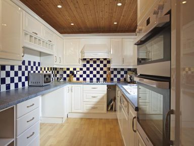 A kitchen with white cabinets blue and white checkered backsplash and wooden ceiling at Amberley Dartmouth