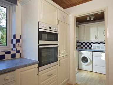A kitchen area with built-in double ovens next to a room with a washing machine and dryer at Amberley in Dartmouth