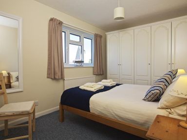 A bedroom with a bed towels on it a window with a model sailboat a chair a mirror and white wardrobes at Amberley in Dartmouth