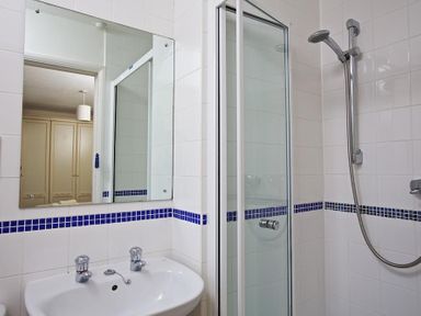 A bathroom with a white sink and two taps a glass shower enclosure and a mirror with blue tile accents at Amberley in Dartmouth