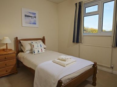 A single bed with folded towels a bedside table with a lamp a window with curtains and a framed picture on the wall at Amberley in Dartmouth