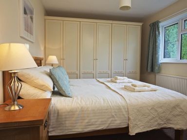 A bedroom with a double bed bedside tables lamps and a row of wardrobes at Amberley in Dartmouth
