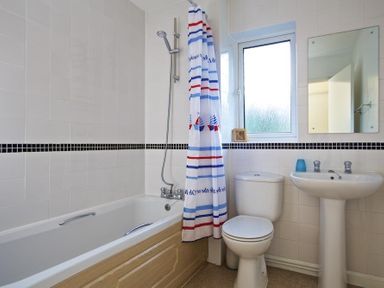 A bathroom with a bathtub shower combination with a striped shower curtain toilet sink and a window at Amberley in Dartmouth