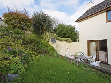 A garden with a grassy area and shrubs next to a house with white walls and sliding glass doors at Amberley in Dartmouth
