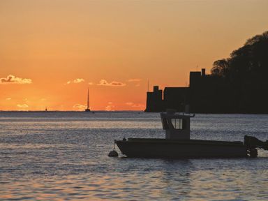 A boat on water at sunset with a castle silhouette and trees in the background at Amberley in Dartmouth