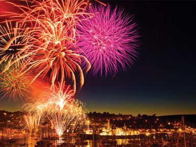 Fireworks lighting up the night sky over a harbor with boats and illuminated buildings at Amberley in Dartmouth