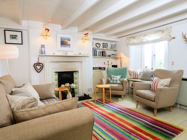 A living room with armchairs a sofa a fireplace and a multicolored striped rug at Bow Cottage in East Portlemouth