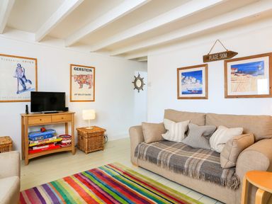 A living room with a beige sofa with cushions a colorful striped rug a wooden TV stand with games and a lamp at Bow Cottage in East Portlemouth