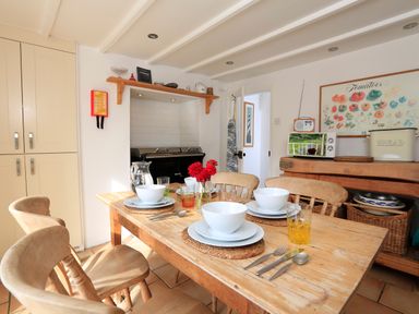 A dining table set with bowls and glasses in a kitchen with wooden chairs and a pantry at Bow Cottage in East Portlemouth
