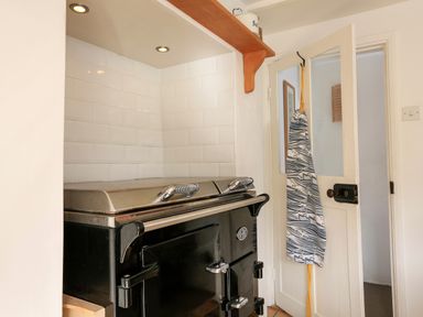 A black oven with silver handles in a kitchen corner with white tiled walls and a door with an apron hanging on it at Bow Cottage in East Portlemouth