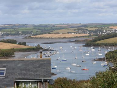 A river with boats anchored near grassy hills and farmland with a house roof in the foreground at Bow Cottage in East Portlemouth