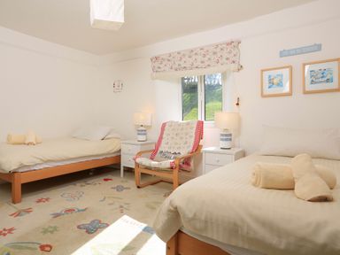 A bedroom with two single beds a chair a window and two nightstands at Bow Cottage East Portlemouth