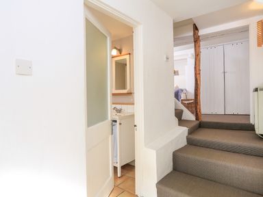 A hallway with carpeted stairs leading to a room with closed white double doors and a partially open door showing a small bathroom sink at Bow Cottage in East Portlemouth