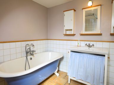 A bathroom with a blue clawfoot bathtub a white sink with a blue curtain and wall cabinets at Bow Cottage in East Portlemouth