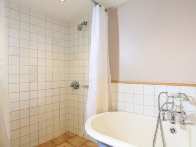 A bathroom with a tiled shower area and a bathtub with chrome fixtures at Bow Cottage in East Portlemouth