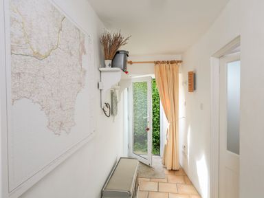 A narrow hallway with a large map on the wall a door with yellow check curtains and a small bench in Bow Cottage East Portlemouth